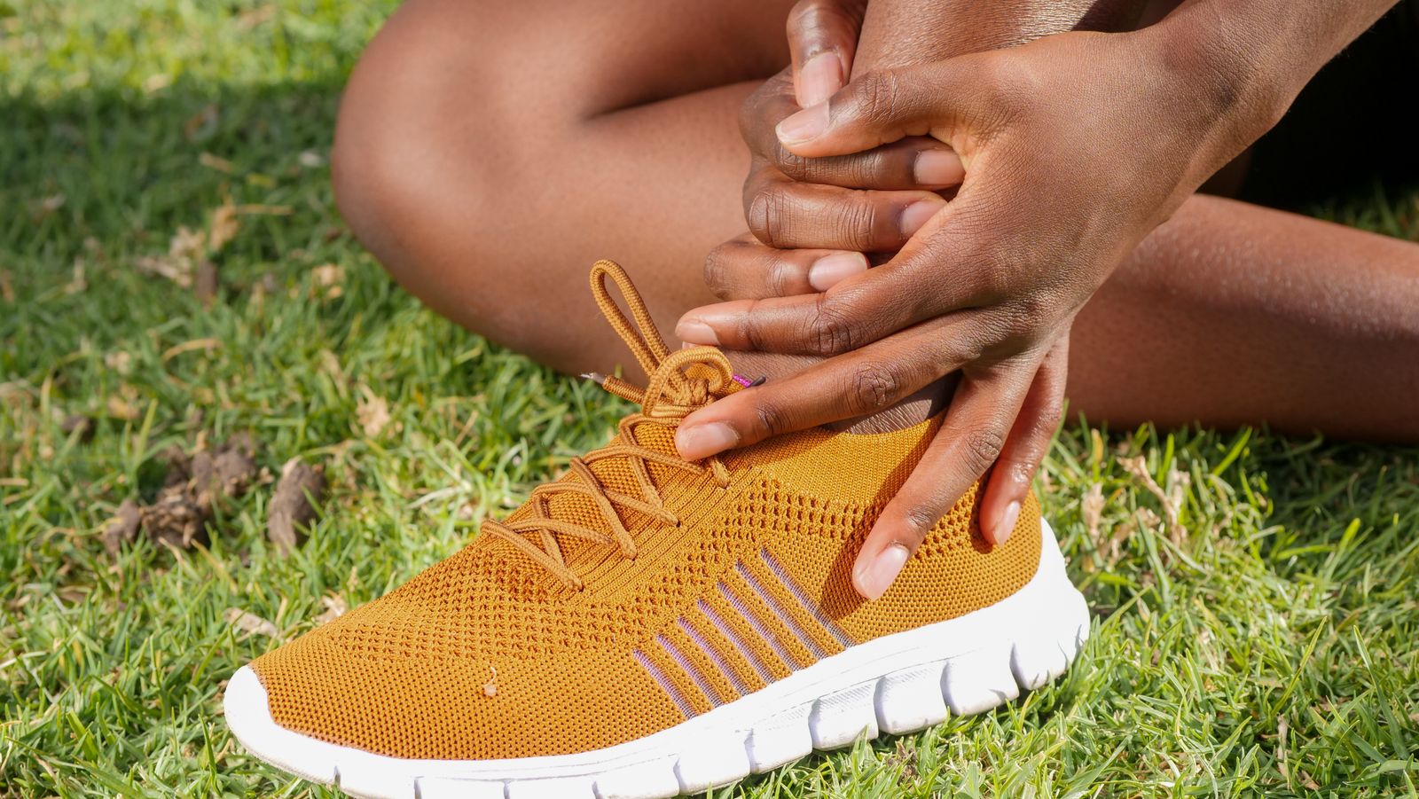 Runner holding the ankle outdoors, matching ankle ligament support and stability decisions.
