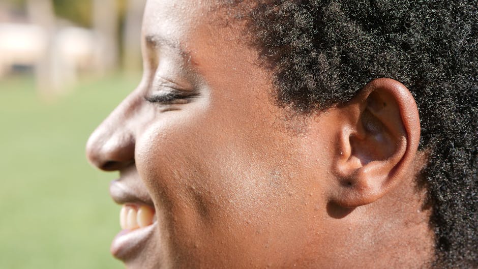 A close-up side profile of a smiling person, showcasing facial features outdoors.