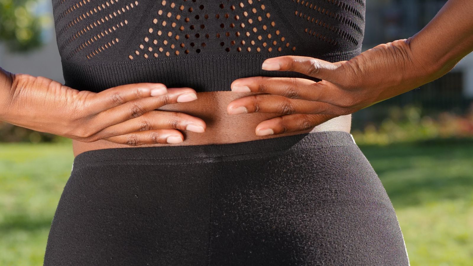 Woman gripping her lower back outdoors in pain, illustrating sciatica nerve discomfort