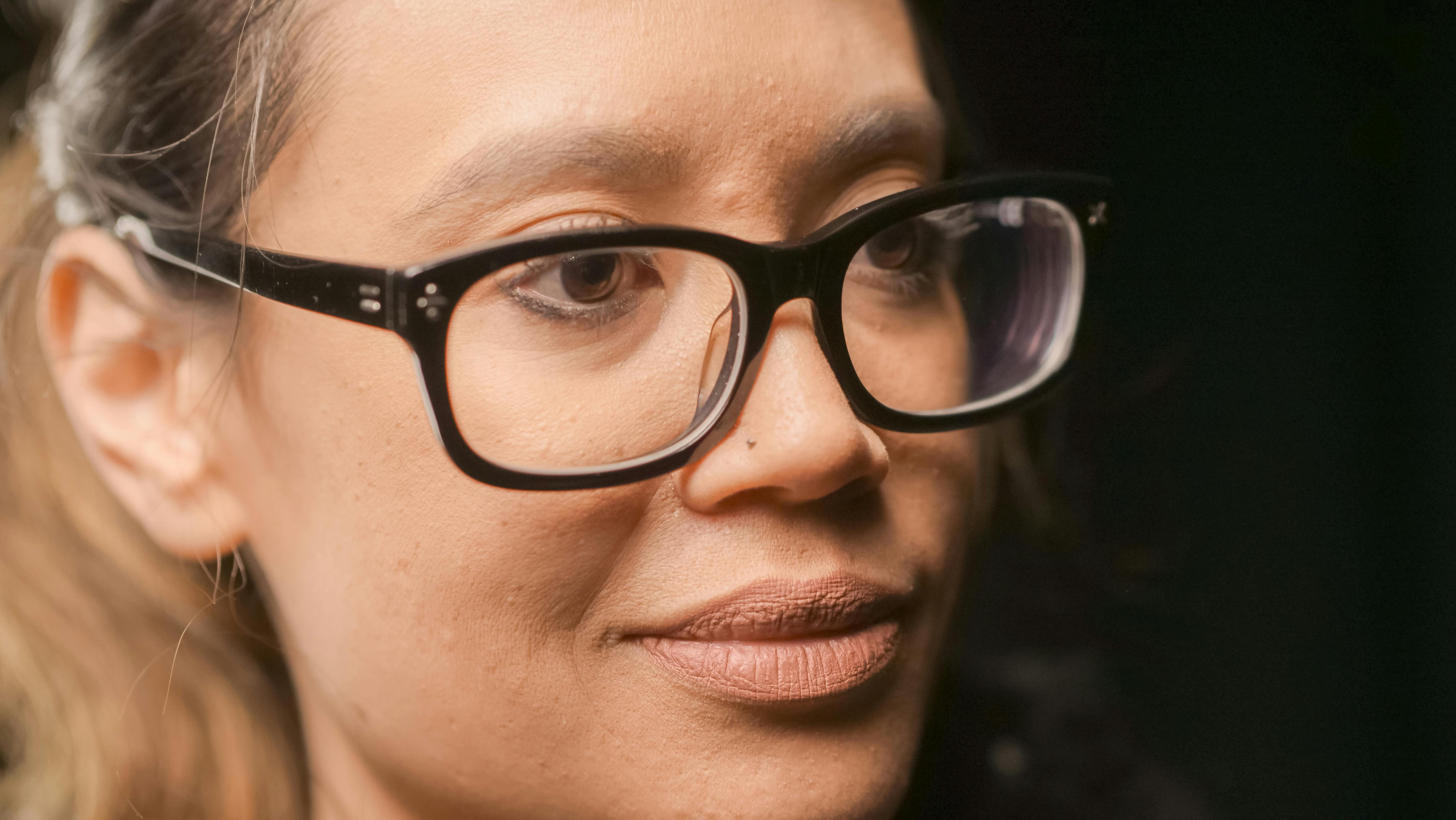 A focused close-up of a woman wearing thick black eyeglasses.