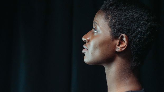 A thoughtful side profile portrait of a woman with afro hair against a dark background.