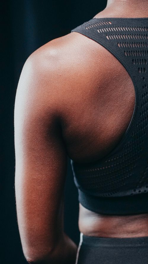Free Detailed view of a person's back shoulder wearing a black sports bra during a workout. Stock Photo