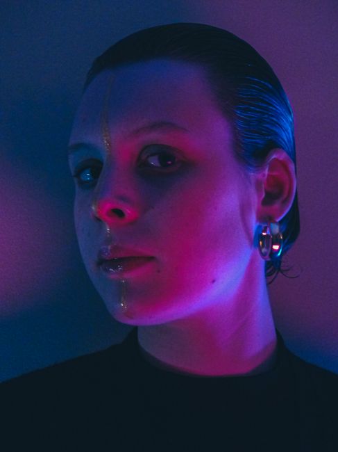 A creative portrait of a person illuminated by vibrant purple and blue lighting in a studio setting.