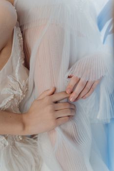 A close-up of bridal hands gently holding a white tulle fabric with delicate embroidery and lace details.