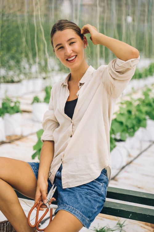 Free A woman smiling in a greenhouse environment, posing with gardening tools, showcasing sustainable farming. Stock Photo