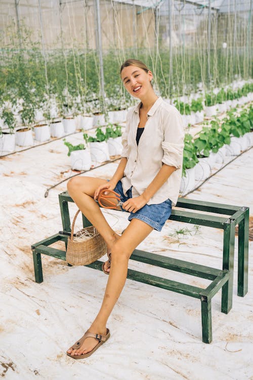 Woman in White Top and Blue Denim Shorts Sitting on Brown Wooden Bench