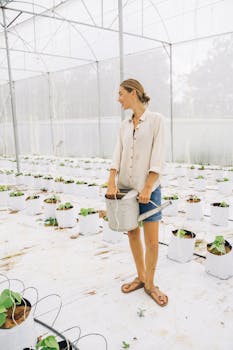 A woman in a greenhouse waters plants with care, promoting sustainable indoor farming.