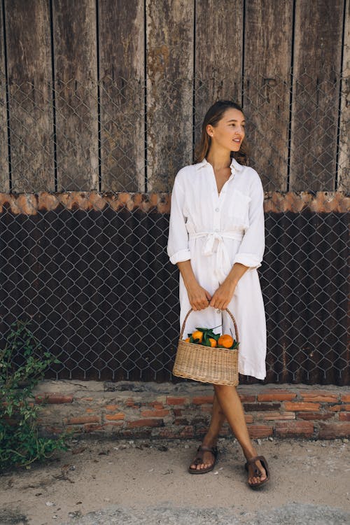 Woman in White Button Up Long Sleeve Shirt and Brown Skirt Standing Beside Gray Metal Fence