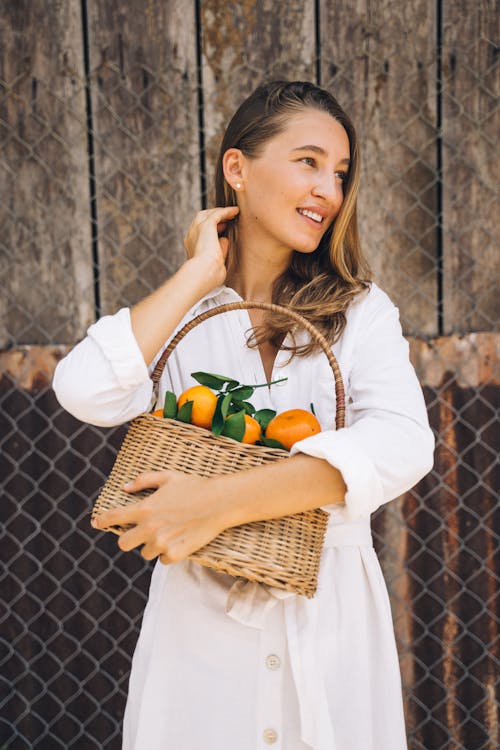 Woman in White Long Sleeve Shirt Holding Brown Woven Basket