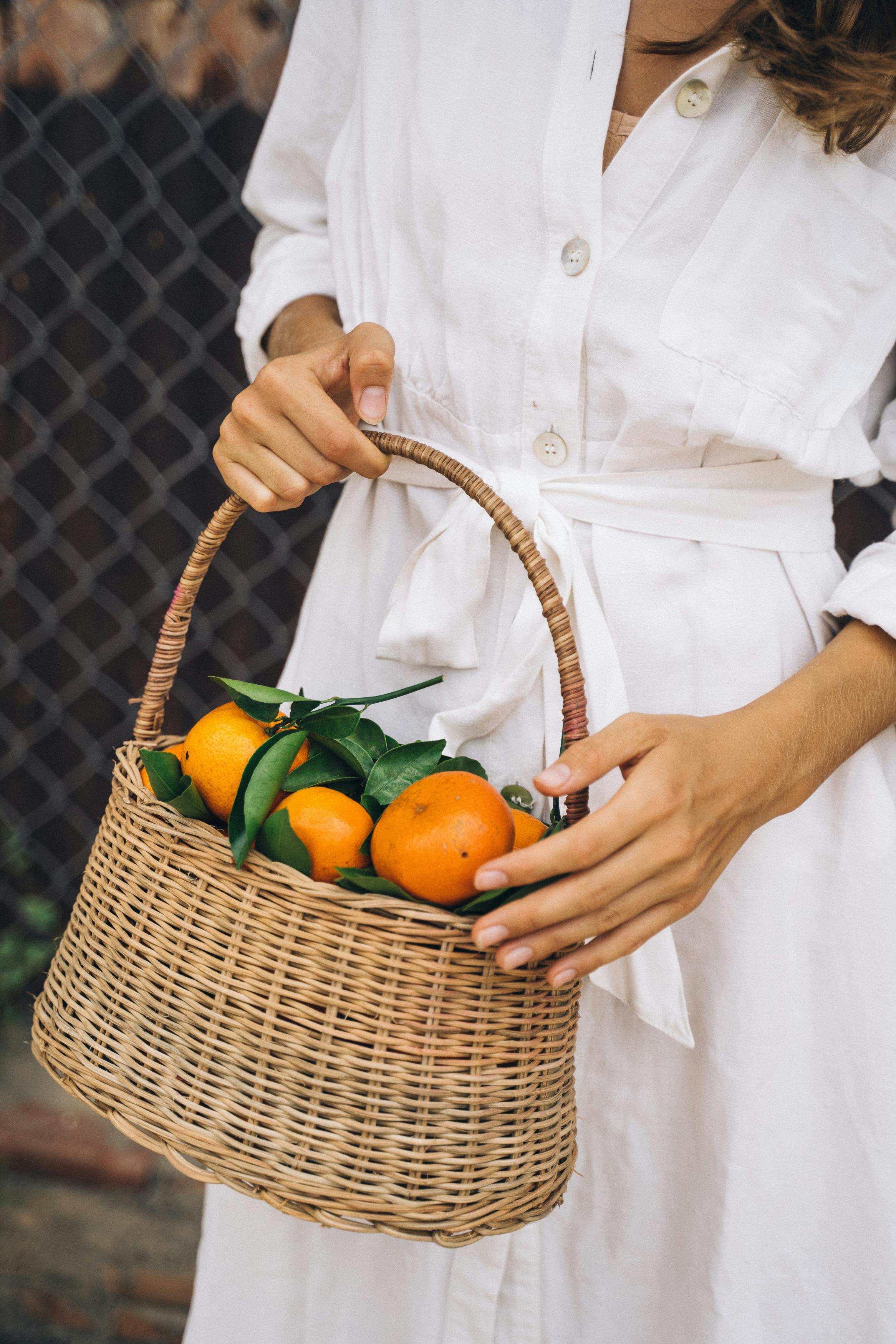 person holding brown woven basket with orange fruits