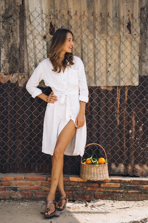 Woman in White Long Sleeve Dress Standing Beside Brown Wooden Fence
