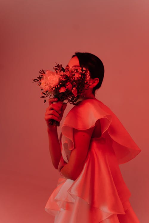 Woman in Dress Covering Face With Bouquet of Flowers