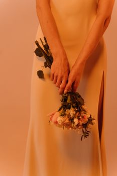 A woman in a long dress gracefully holds a bouquet of flowers, embodying elegance and subtlety indoors.