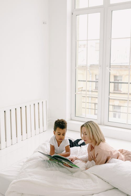 Free Mother and Son Reading Book Together while Lying on Bed Stock Photo