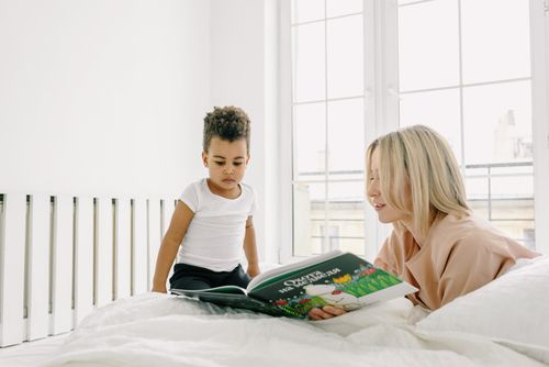 Free A mother reading a book to her child on a bed, fostering early learning and bonding. Stock Photo