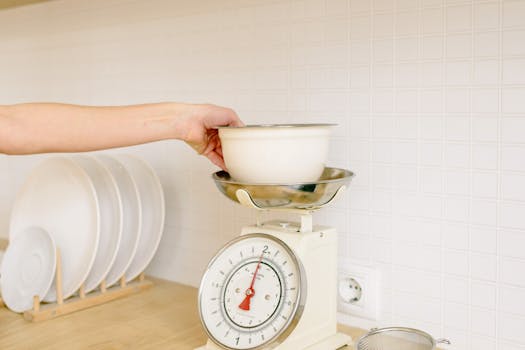 Close-up of hand placing a bowl on a kitchen weighing scale for food preparation.