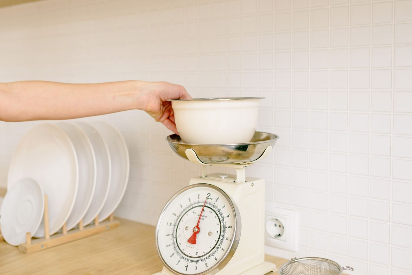 A bowl being weighed on a kitchen scale while baking ingredients are prepared