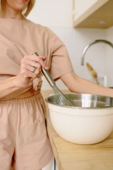 Close-up of a woman whisking ingredients in a bowl in a modern kitchen setting.