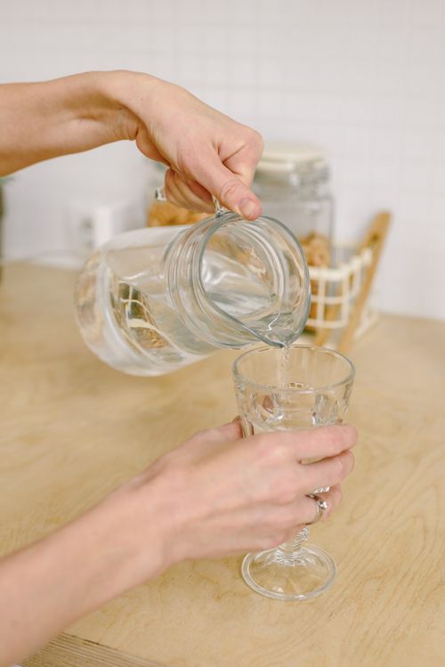 Free A close-up view of hands pouring water from a pitcher into a glass indoors. Stock Photo