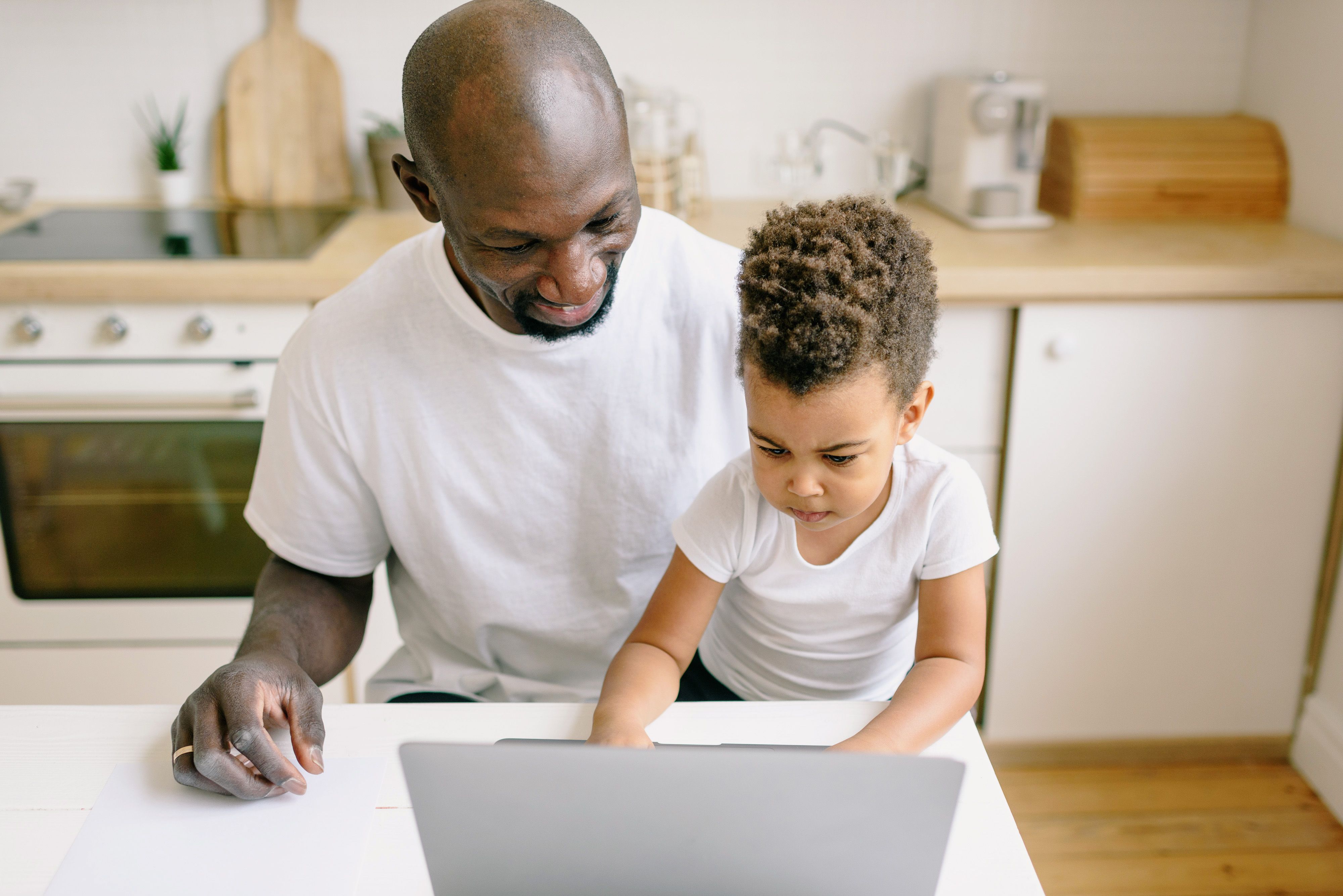 Father and young child use a laptop together at the kitchen table at home