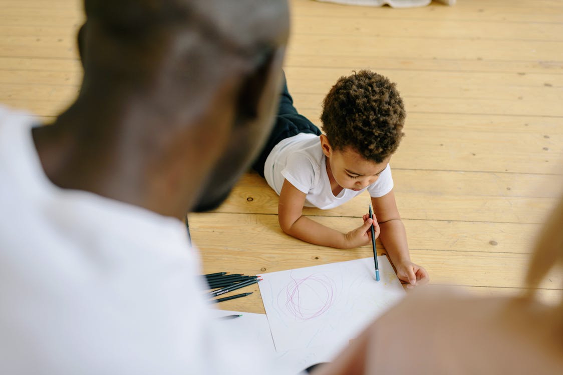 A Boy Holding a Pencil and Paper Lying on Wooden Floor