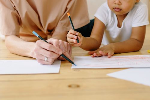Free A woman and child drawing with color pencils on white paper around a table indoors. Stock Photo