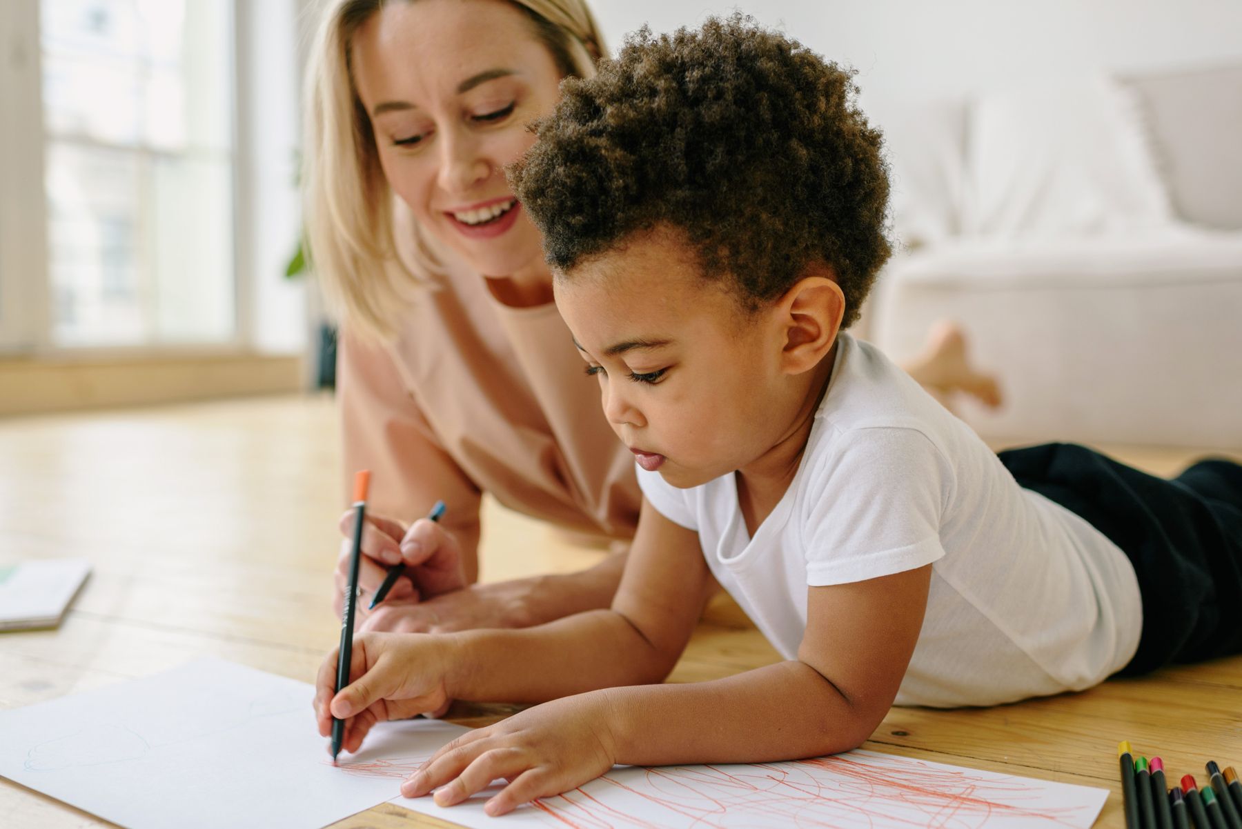 A mother and child lying on the floor and drawing together with colored pencils on paper