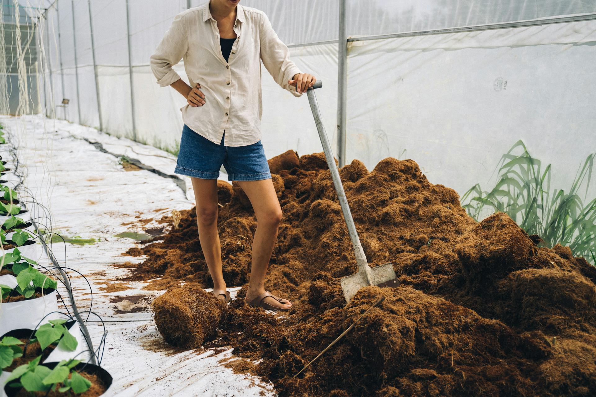 Person working in an indoor farm with compost using a shovel, promoting sustainable agriculture.