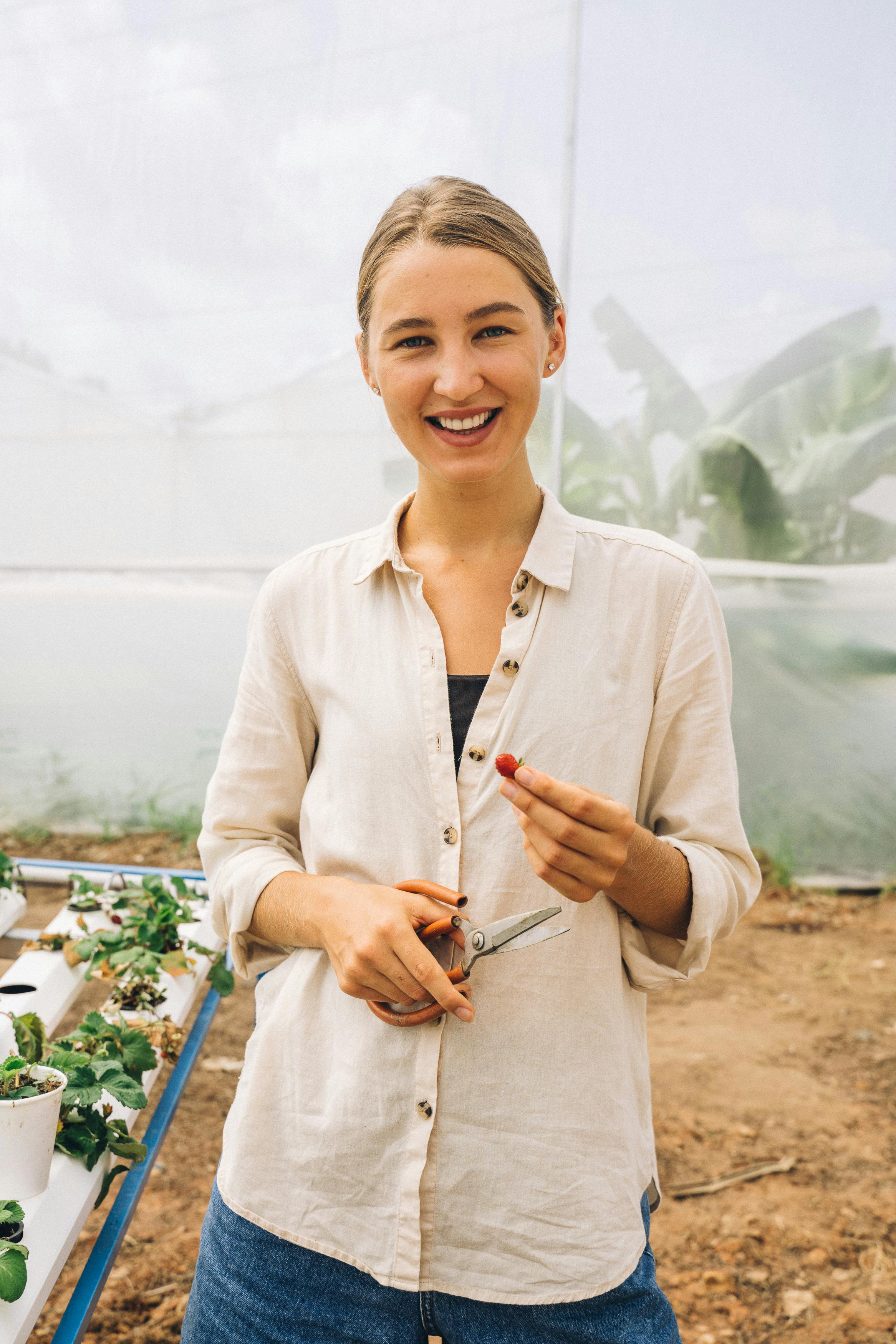 A happy horticulturist holding pruning shears inside a greenhouse.