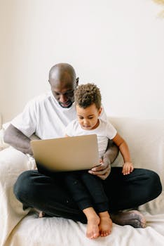 A heartwarming moment of a father and son bonding together while using a laptop at home.