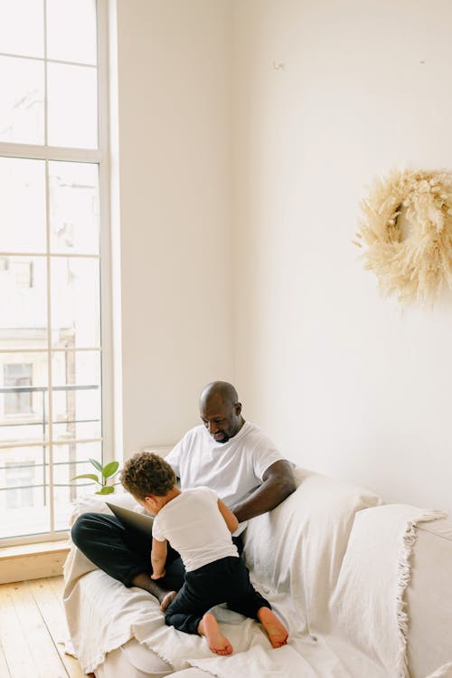 Free Father and Son Sitting on a Couch while Spending Time Together Stock Photo