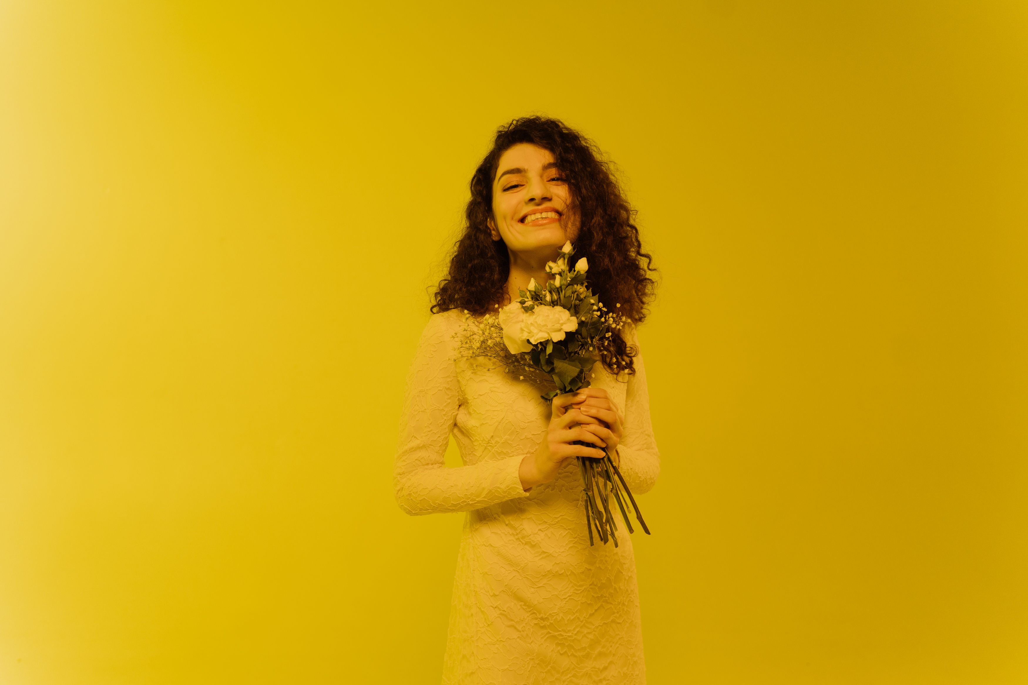 Woman in White Long Sleeves Dress Holding a Bunch of Flowers Smiling ...