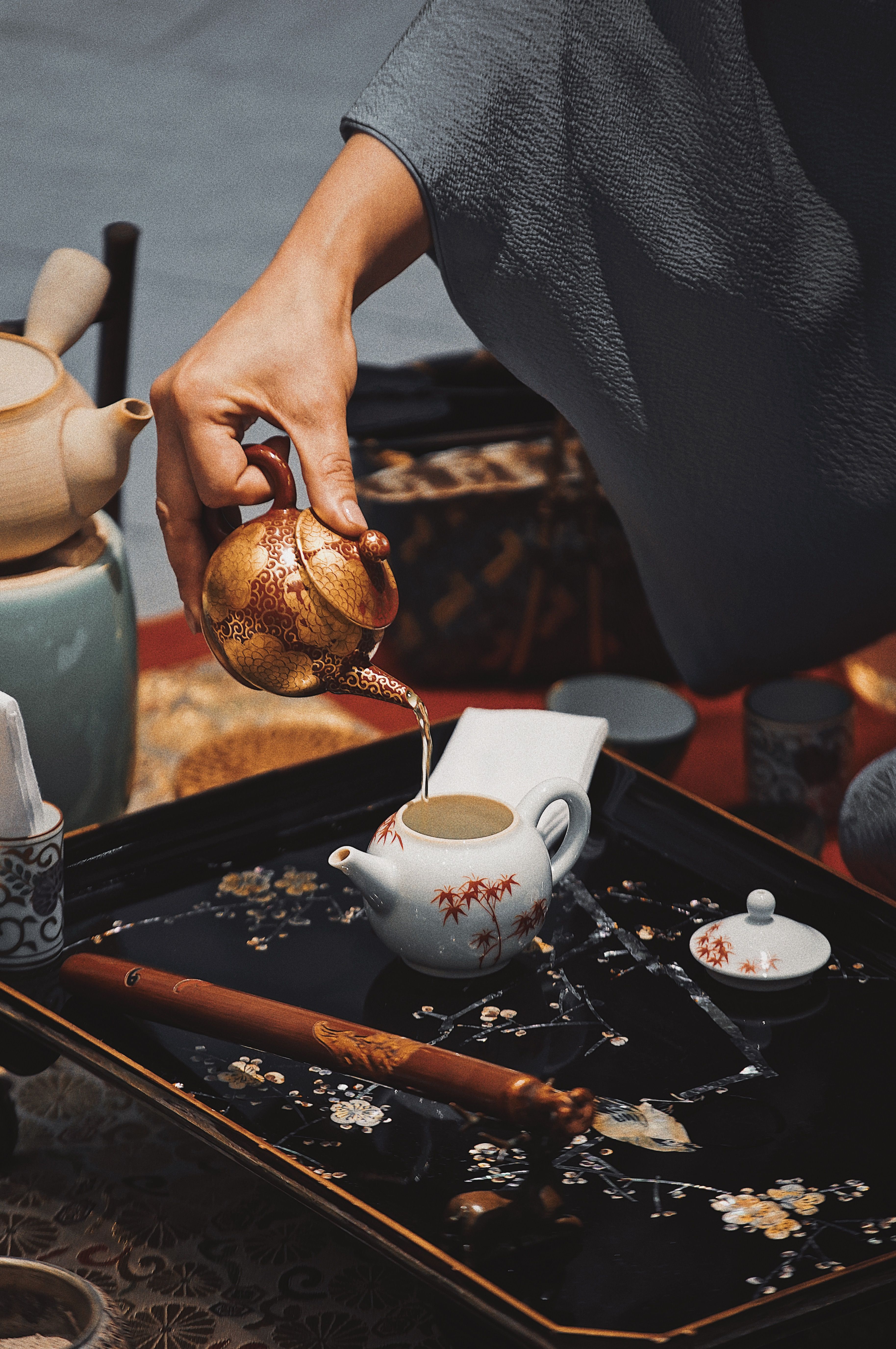 Close-up of a hand pouring tea from an ornamented kettle into a ceramic pot during a traditional outdoor ceremony.