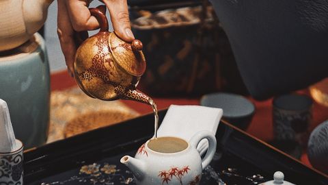 Close-up of a hand pouring tea from an ornamented kettle into a ceramic pot during a traditional outdoor ceremony.