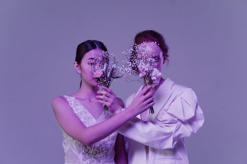 Free Artistic portrait of a same-sex couple holding bouquets against a violet background. Stock Photo