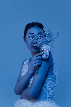 Portrait of a woman holding flowers, captured with ethereal blue lighting for a dreamy effect.