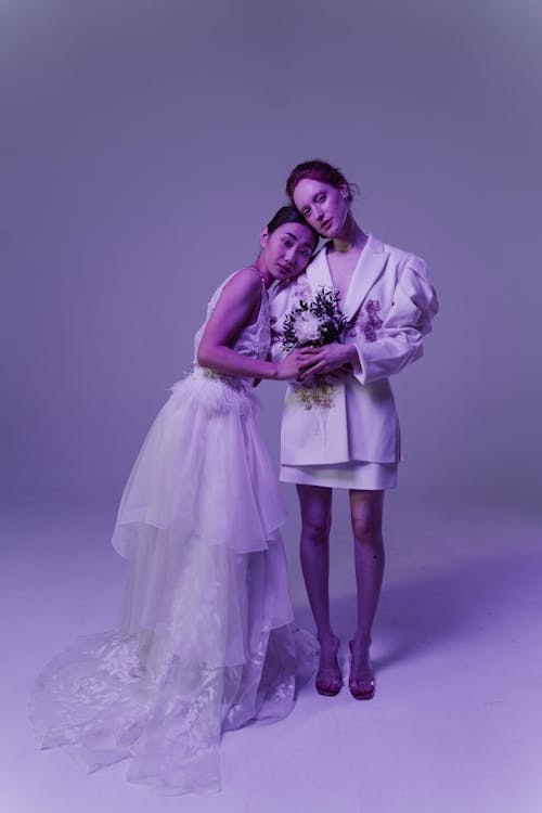 Women in White Dresses Posing Together Holding a Bouquet of Flowers