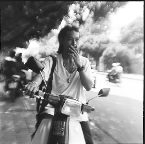 Free Grayscale Photo of a Man Smoking a Cigarette while Sitting on a Motorcycle Stock Photo