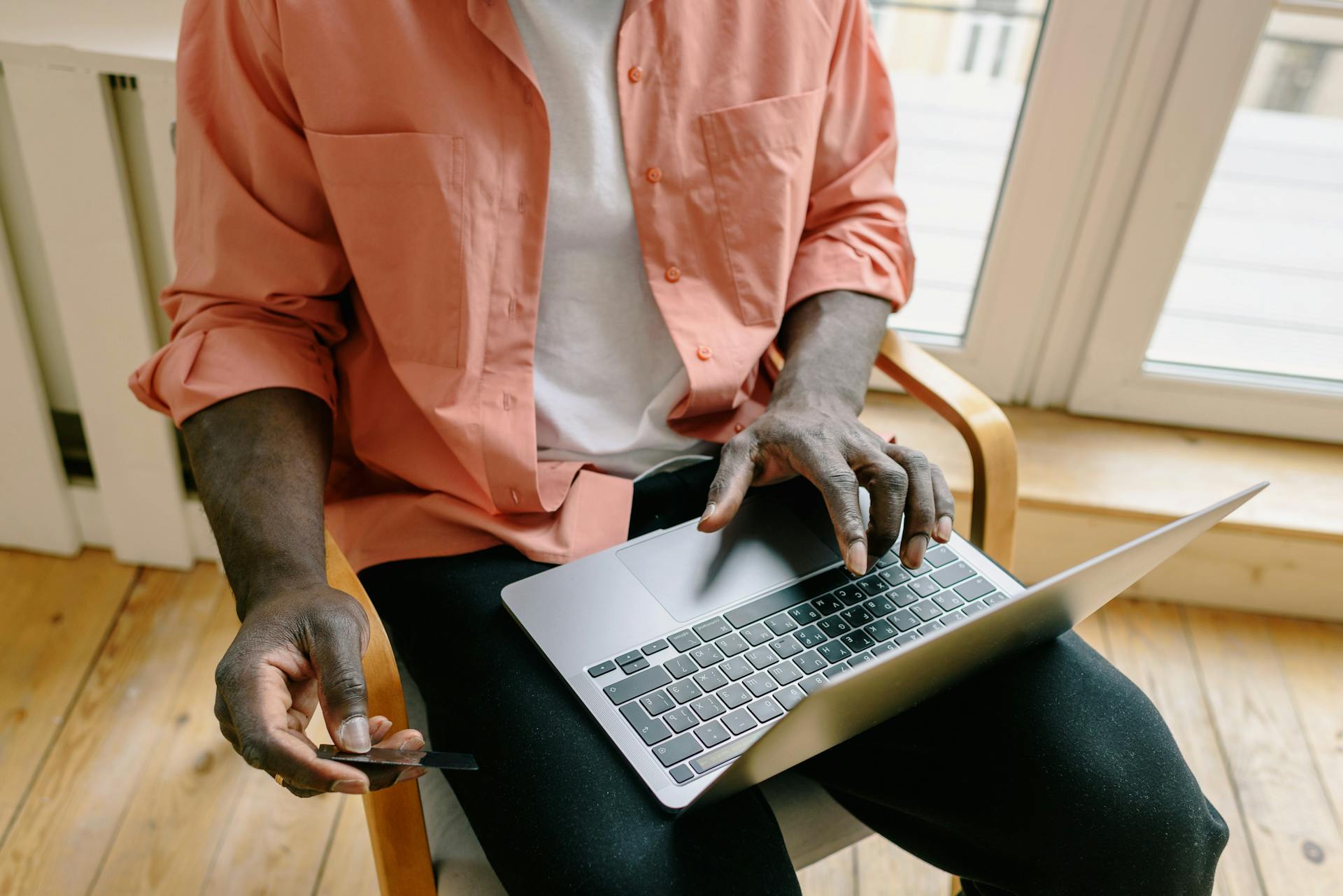 A man uses a laptop and credit card for online shopping in a home setting, reflecting modern cashless transactions.