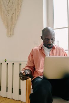 A man in a pink shirt focused on online shopping using his laptop in a cozy home setting.