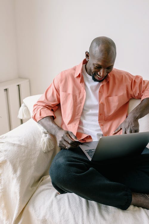Free A man sits comfortably on a couch using a laptop for online shopping in a cozy home setting. Stock Photo