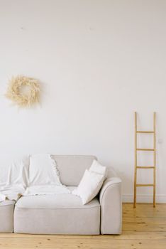 Modern living room showcasing a beige sofa, decorative ladder, and dried flower wreath in a minimalist style.