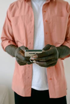 A man in a pink shirt using a smartphone indoors, showcasing casual modern lifestyle.