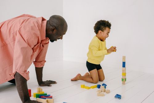 Free A joyful moment between a father and son playing with colorful wooden blocks on the floor at home. Stock Photo