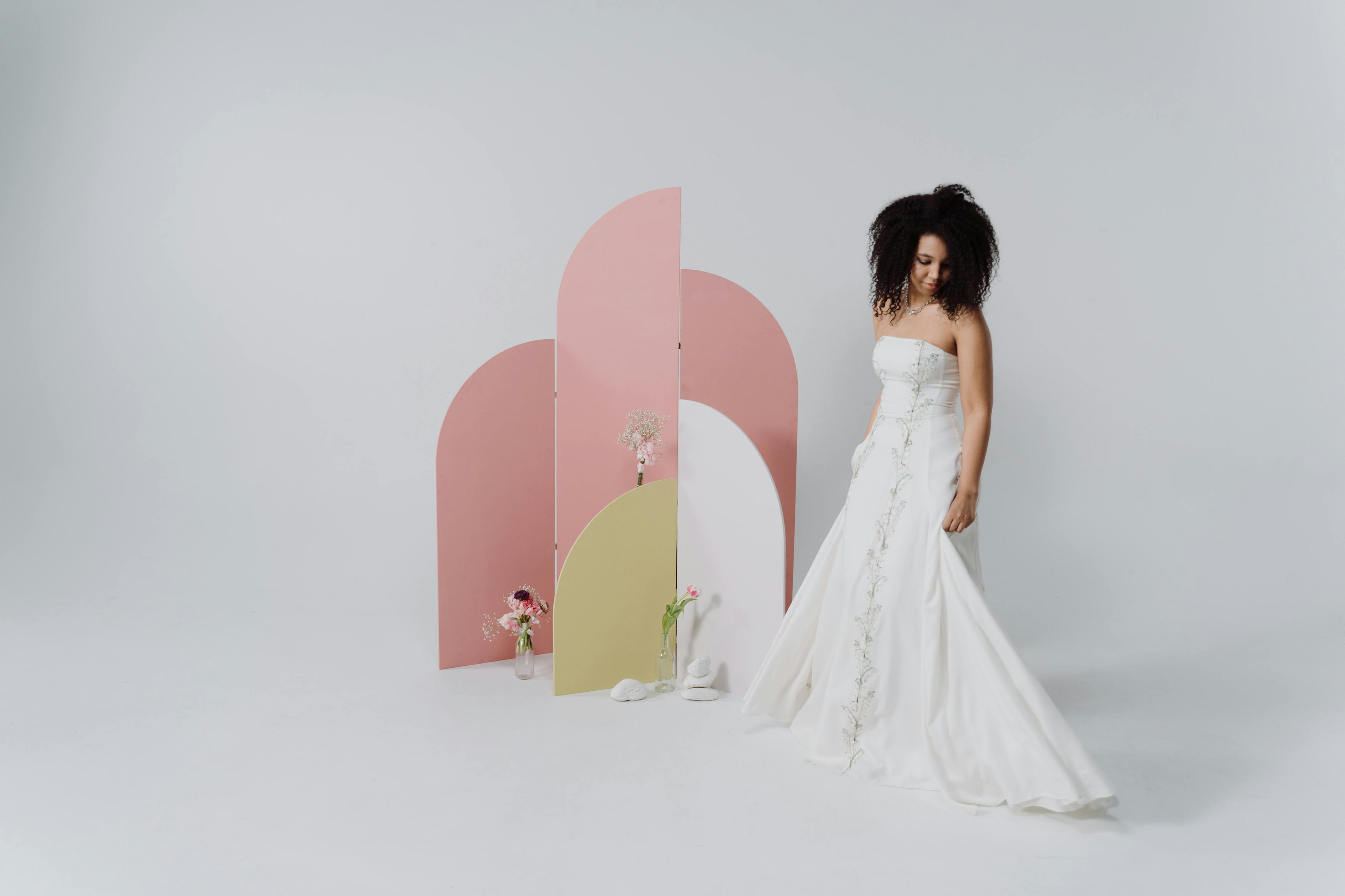 A bride in a white dress poses with a modern pastel backdrop, exuding elegance and style.
