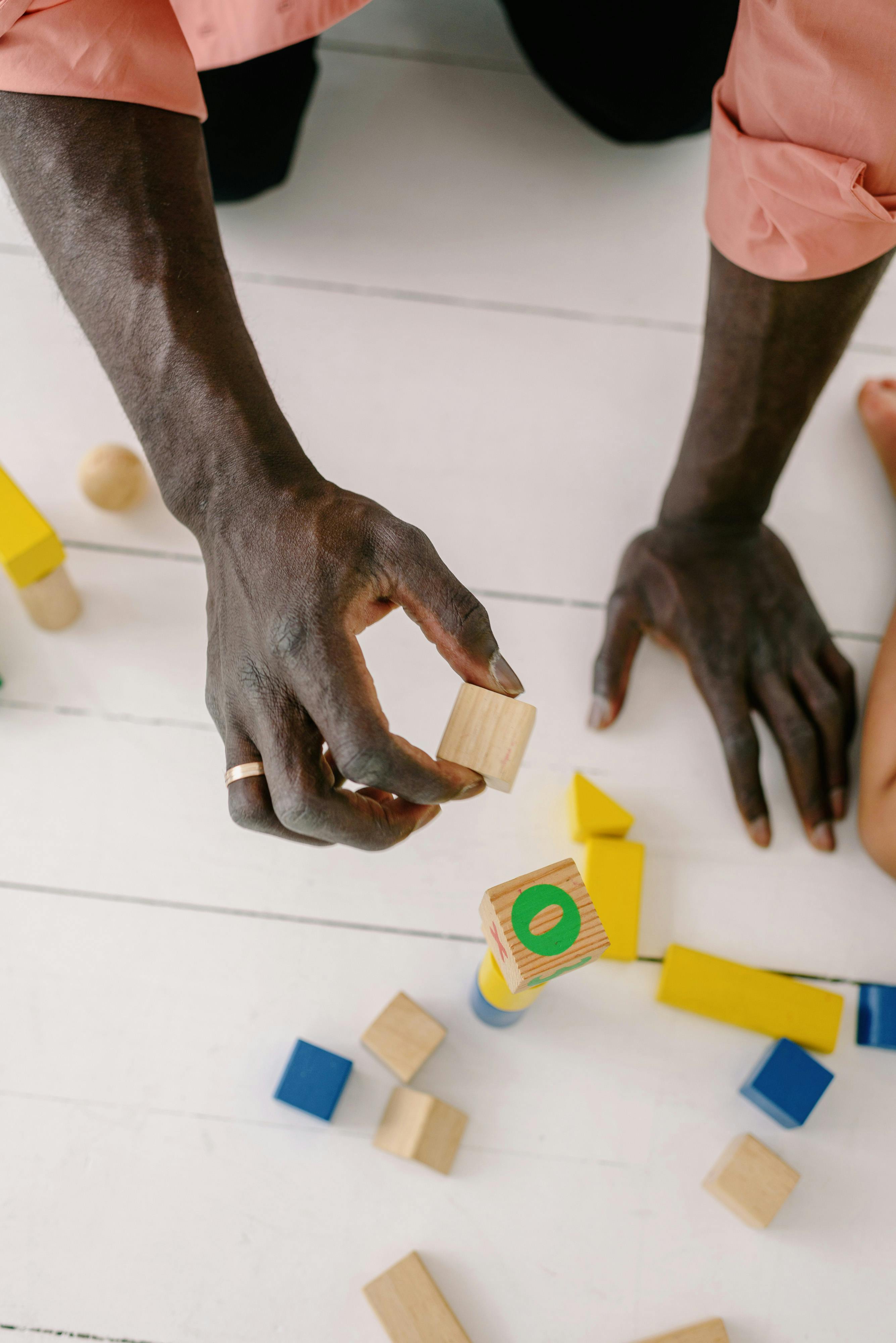 Close-up of hands arranging colorful wooden blocks on a white floor indoors.