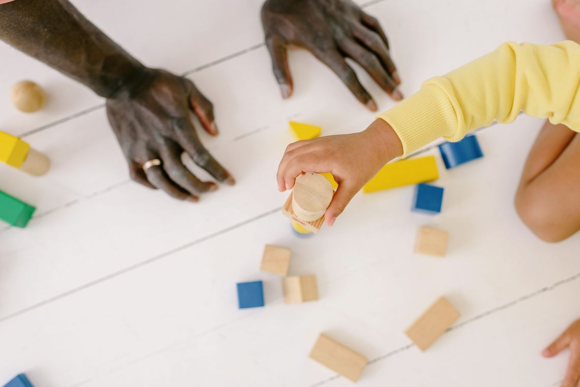 Parent and child building together with wooden blocks on the floor