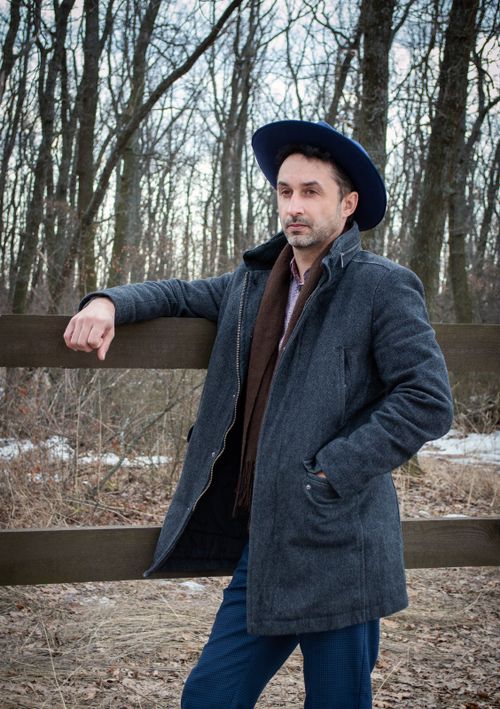 Free Confident adult male wearing warm clothing while standing near wooden barrier in autumn lumber on cloudy day Stock Photo