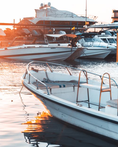 Free Tranquil marina scene with yachts and motorboats moored at sunset, reflecting warm colors on water. Stock Photo