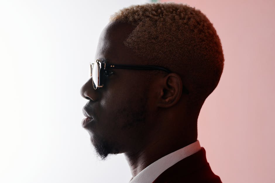 Stylish side profile portrait of a man wearing sunglasses in a studio setting. Neutral background.